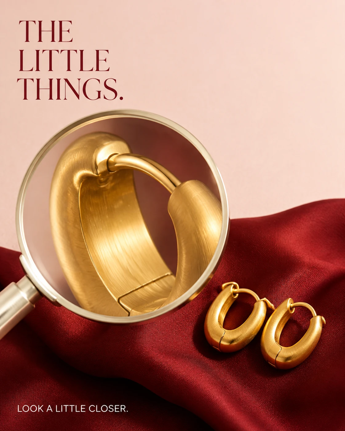 Magnifying glass revealing gold earring texture and closure on cherry-red silk.